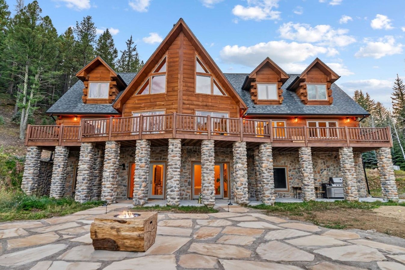 A log cabin with a stone foundation, multiple balconies, and a stone fire pit.