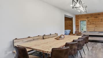 Un espace repas moderne avec une grande table en bois, des chaises en cuir et un luminaire suspendu aux motifs géométriques.