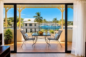 A balcony with a view of a pool, two chairs, a table with a bowl of fruit and a bottle, and a potted plant. - Palmer Street Stay - Steps from Townsville CBD (South Townsville)