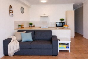 A living room with a dark grey sofa, a white side table with books, a microwave, and a small plant on the counter. - Palmer Street Stay - Steps from Townsville CBD (South Townsville)