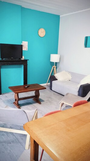 A living room with a teal wall, a wooden coffee table, a grey sofa, a television, and a lamp. - Laverie de François, wifi, commerce, 6pers, Aréna (Liévin)