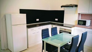 A compact kitchen with a refrigerator, microwave, stove, and a glass-top dining table with chairs. - Laverie de François, wifi, commerce, 6pers, Aréna (Liévin)