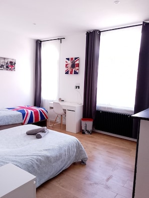 Hotellihuone, jossa on kaksi sänkyä, työpöytä, tuoli ja patteri.