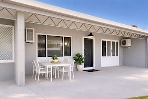 A house with a covered patio, a dining table with chairs, a potted plant, and an air conditioning unit. - Convenient Townsville Stay Near Hospital and CBD (Pimlico)