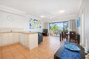 A modern kitchen with a dining area, a balcony with a view of palm trees, and a ceiling fan. - Marina View 1 BR 1BA Apartment Townsville (South Townsville)