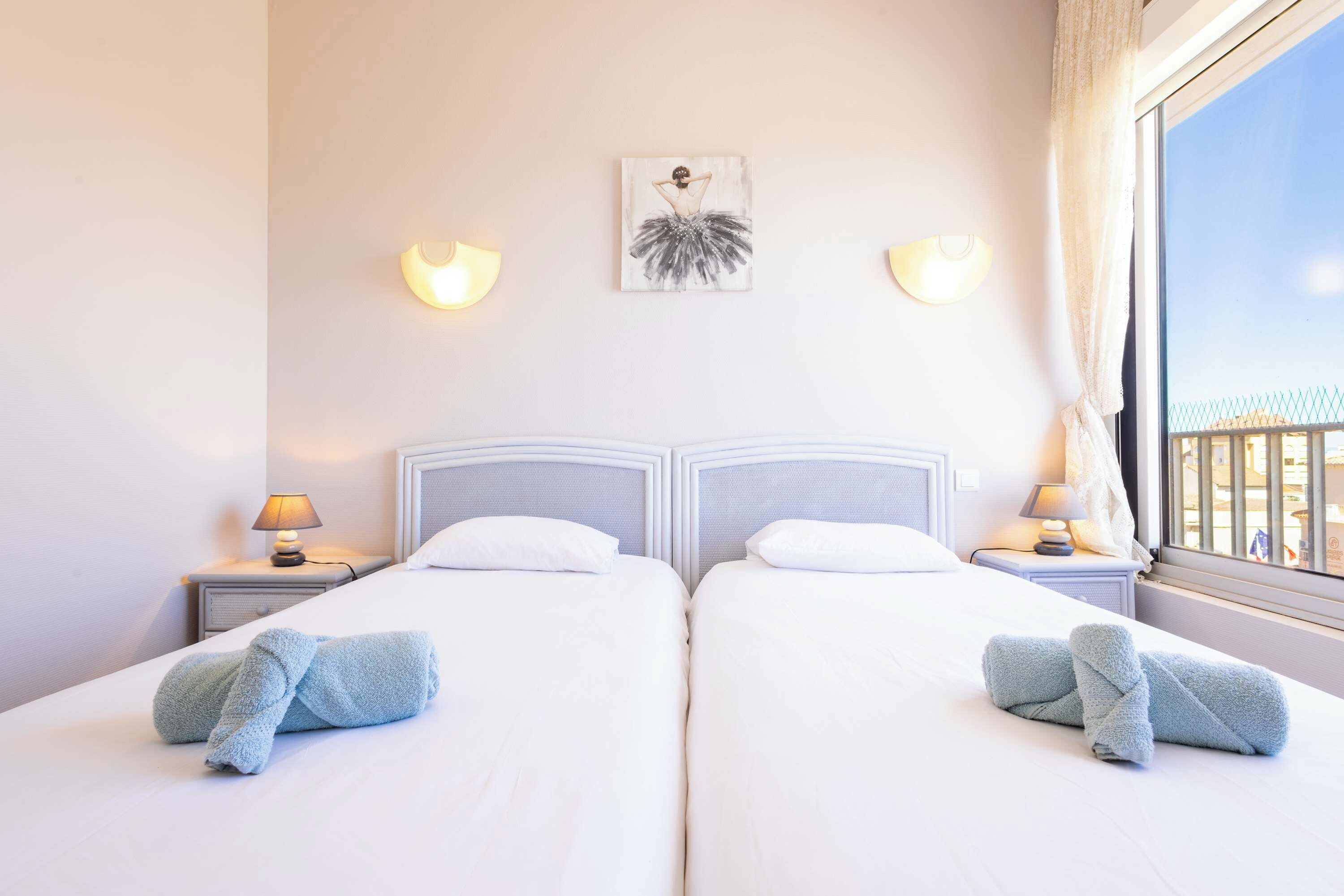A hotel room with two beds, a painting on the wall, and a window with a view.