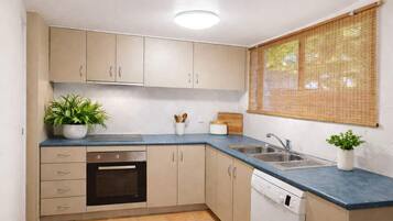 A compact kitchen with beige cabinets, a built-in oven, a dishwasher, and a sink. There are two potted plants on the counter.