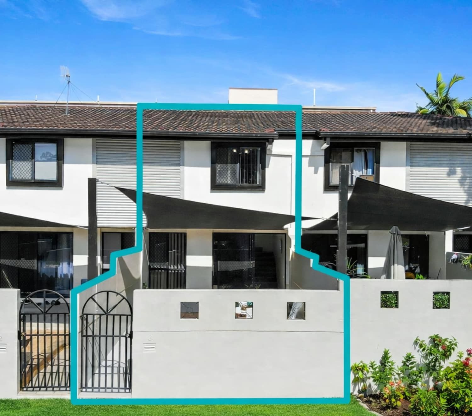 A two-story residential building with a tiled roof, a gated entrance, and outdoor umbrellas.