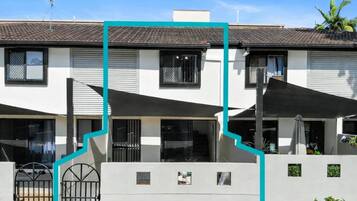 A two-story residential building with a tiled roof, a gated entrance, and outdoor umbrellas.