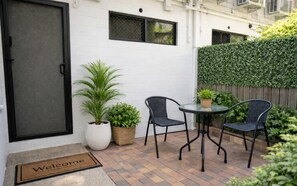 Eine Terrasse mit Tisch und zwei Stühlen, einem Blumentopf und einer Fußmatte.