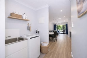 A modern kitchen with a built-in washing machine, a dining area with a view, and a hallway leading to a living space. - Townsville Golf Course Haven 2 Bed 2 Bath with Secure Parking (Heidelberg)