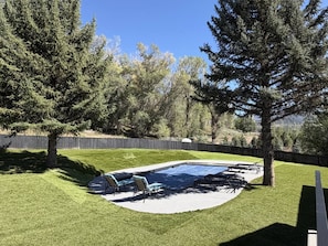A backyard with a swimming pool, lounge chairs, and a wooden fence. - Mt. Sopris Views | Pool | 3BR Mountain Retreat (Carbondale)