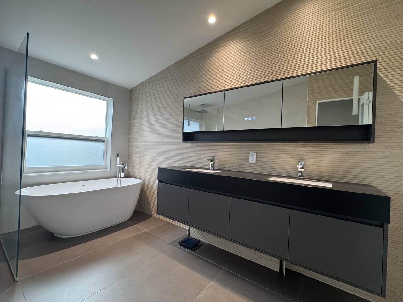 A modern bathroom with a freestanding bathtub, a large mirror, and a dark-toned vanity.