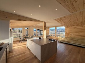 A modern kitchen with a central island, wooden flooring, and large windows offering a city view. - Mt. Sopris Views | Pool | 3BR Mountain Retreat (Carbondale)