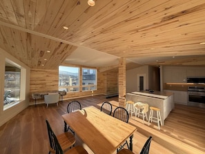 Een ruime kamer met een houten plafond, een eethoek met een grote tafel en stoelen, en een keuken met een centraal kookeiland.