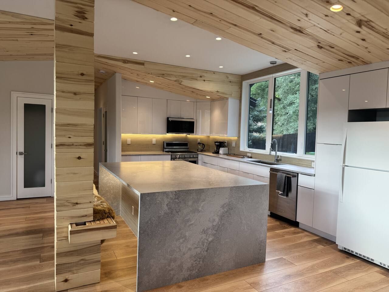A modern kitchen with wooden ceiling beams, a central island, and a large window.