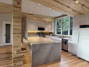 A modern kitchen with wooden ceiling beams, a central island, and a large window. - Mt. Sopris Views | Pool | 3BR Mountain Retreat (Carbondale)