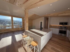A modern kitchen with a central island, wooden flooring, and large windows offering a view. - Mt. Sopris Views | Pool | 3BR Mountain Retreat (Carbondale)