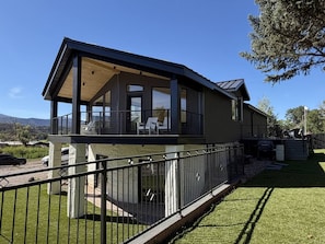 A modern two-story house with a balcony, a fenced yard, and a clear view of the surrounding landscape. - Mt. Sopris Views | Pool | 3BR Mountain Retreat (Carbondale)