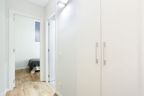Um corredor estreito com uma cama ao fundo, uma porta à esquerda e um guarda-roupa à direita.