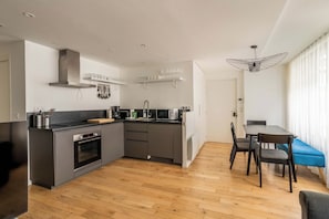 A modern kitchen with grey cabinets, a built-in oven, and a dining area with a blue table and chairs. - The Collection - Bright & renovated 3BD Le Marais! (Paris)