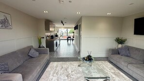 A modern living room with grey sofas, a coffee table, and a kitchen in the background. - Cozy Penthouse - 2 Bedroom in Central Manchester (Manchester)