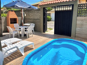 A swimming pool with a tiled edge, surrounded by white plastic lounge chairs and a barbecue area with a brick oven. - Cozy duplex in Porto de Galinhas, 50m from the sea. • Pool • Grill (Ipojuca)