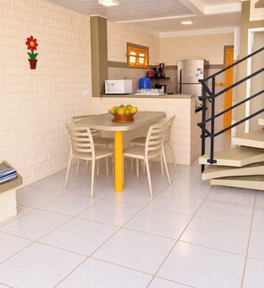 A dining area with a table and chairs, a fruit bowl, a microwave, and a refrigerator. - Cozy duplex in Porto de Galinhas, 50m from the sea. • Pool • Grill (Ipojuca)