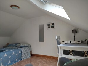 A bedroom with a sloped ceiling, a bed with patterned bedding, a bedside table with a lamp, and a small picture frame on the wall. - Townhouse with a terrace and garden, 180 m from the lock. (Tinténiac)
