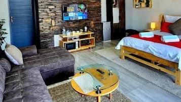 Un vaste espace de vie agrémenté d’un mur en pierre, d’un ensemble de canapés, d’une table basse en bois et d’un lit recouvert d’une couverture rouge.