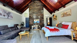 Een gezellige woonkamer met een stenen openhaard, een bank, een bed met rode beddengoed en een televisie.