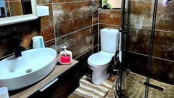 Une salle de bain avec un lavabo rond, des toilettes et une douche à parois de verre.