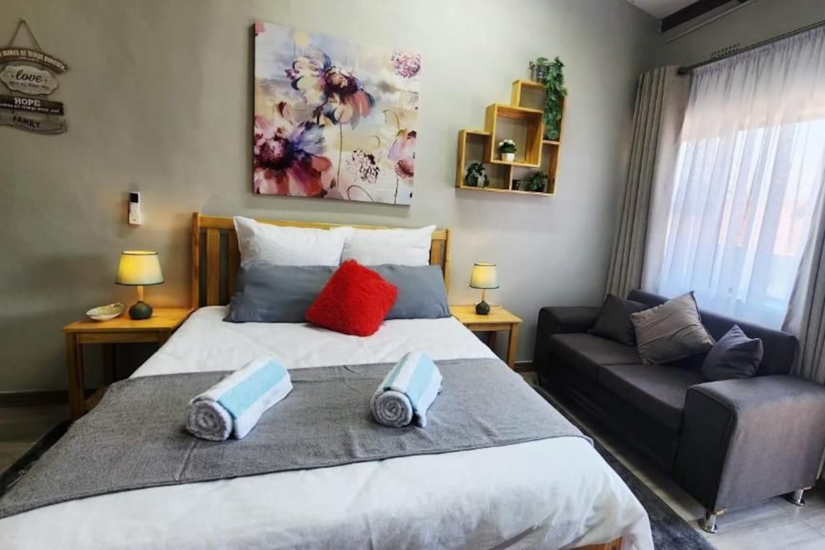 Een hotelkamer met een bed, een bank, een schilderij, een lamp en een plank met planten.