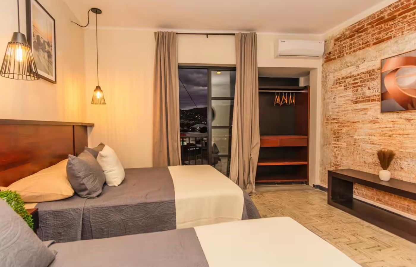 A hotel room with two beds, a closet, a TV, and a view of the city.