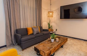 A living room with a grey sofa, yellow cushions, a wooden coffee table, and a hanging light fixture. - 3-Bedroom Apartment with AC Near the Zócalo (Oaxaca de Juárez)