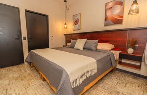 A hotel room with a large bed, a wooden headboard, a nightstand, and a wall-mounted lamp. - 3-Bedroom Apartment with AC Near the Zócalo (Oaxaca de Juárez)