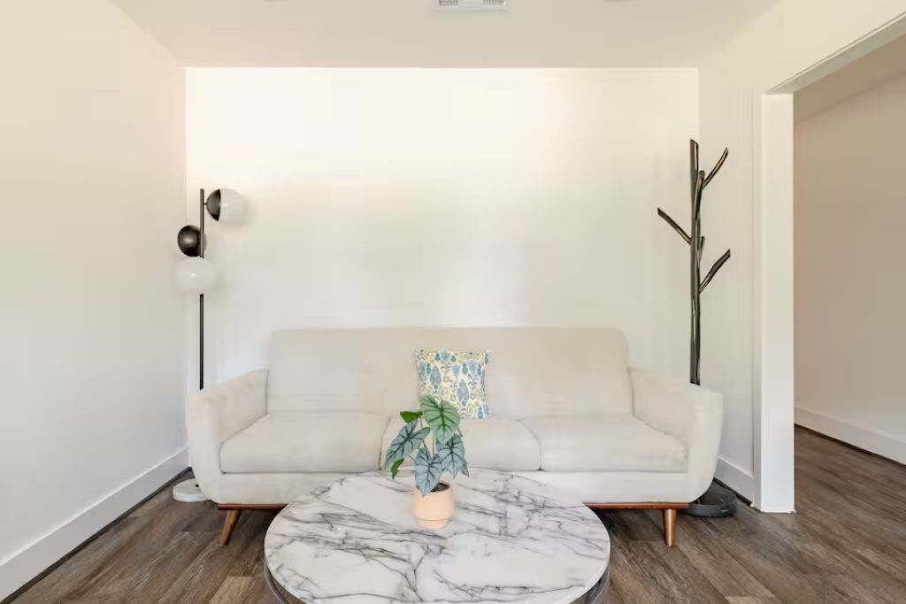 A modern living room with a white sofa, a marble coffee table, and a potted plant.