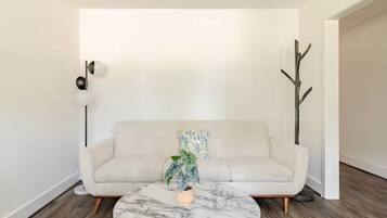 A modern living room with a white sofa, a marble coffee table, and a potted plant.
