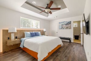 A bedroom with a bed, bedside lamps, a ceiling fan, a window with blinds, a painting on the wall, and a television mounted on the wall. - Modern Oasis 3-bedroom house with AC in quiet Houston neighborhood (Houston)