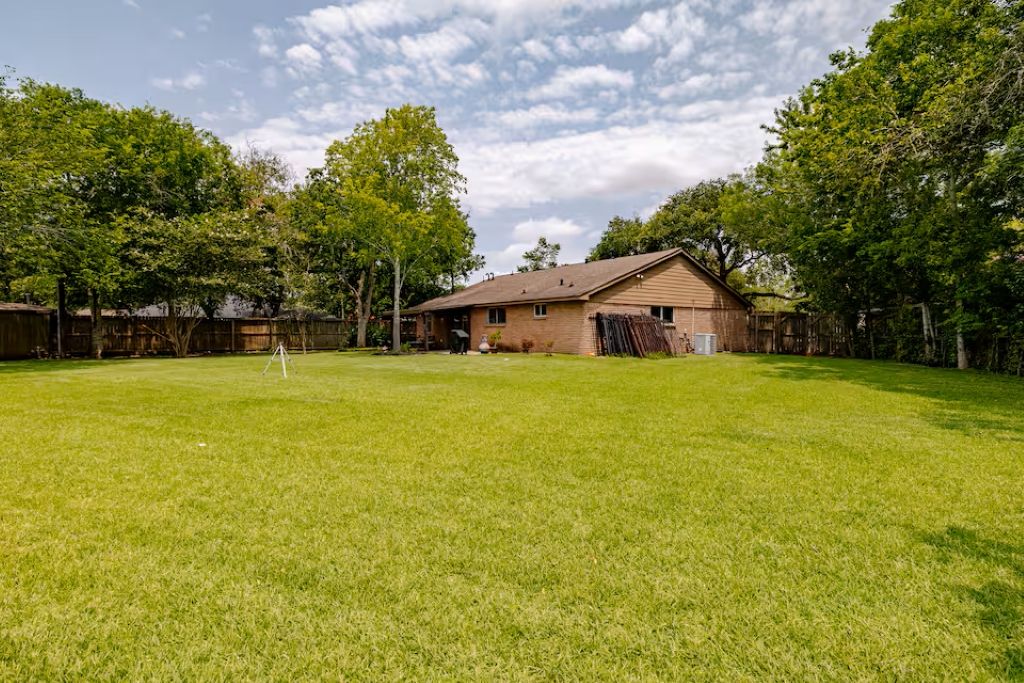 A residential backyard with a brick house, a wooden fence, and a grassy lawn.