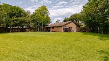 A residential backyard with a brick house, a wooden fence, and a grassy lawn.