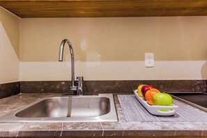 A kitchen with a stainless steel sink, a marble countertop, and a fruit tray with apples and oranges. - Huachinango 34 by Homirent (Cancún)