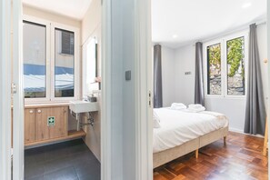 A bedroom with a bed, a window with curtains, a bathroom with a sink, and a wooden cabinet. - Chez Agostinha by Atlantic Holiday (Funchal)
