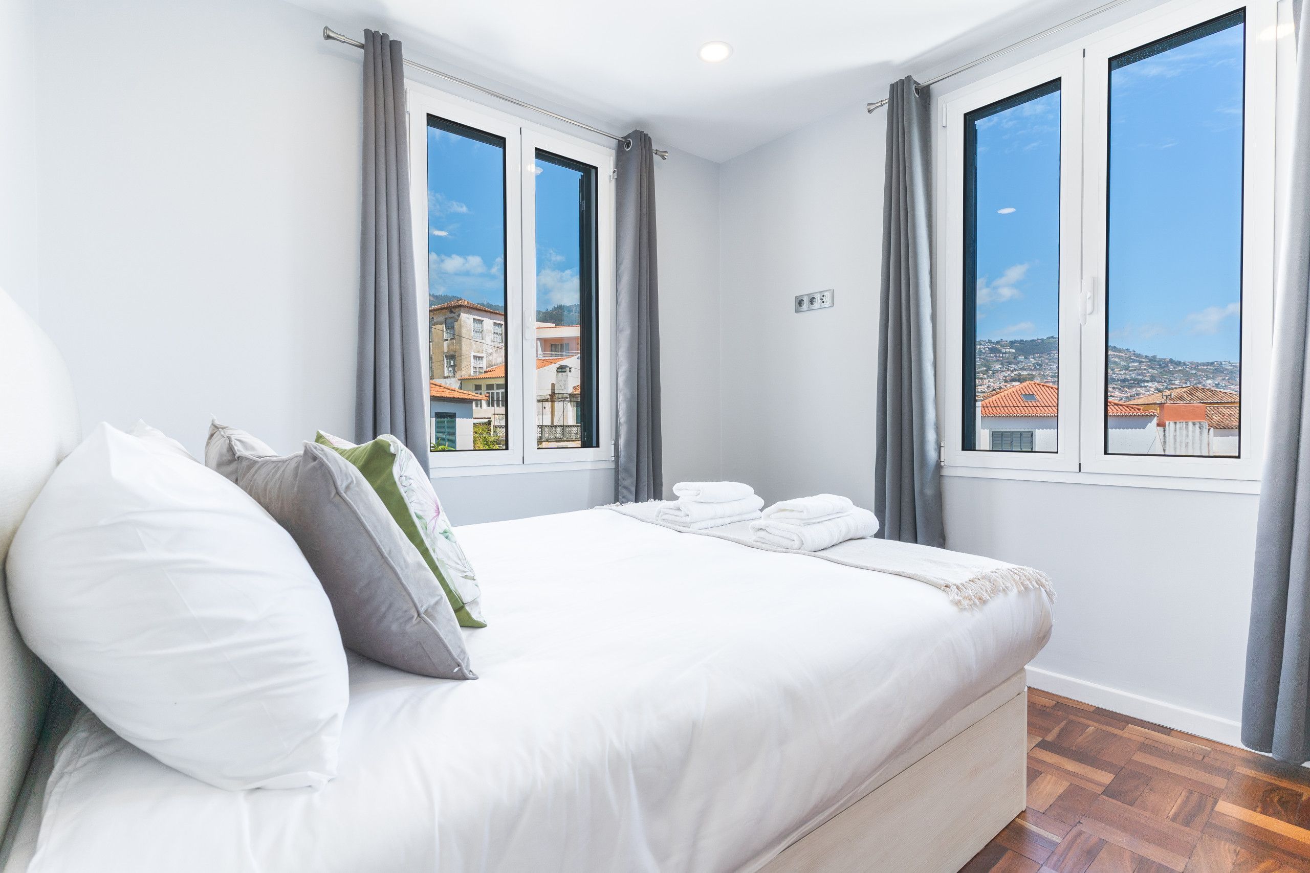 Una habitación de hotel con una cama, dos ventanas y vistas a edificios.