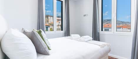 A hotel room with a bed, two windows, and a view of buildings.