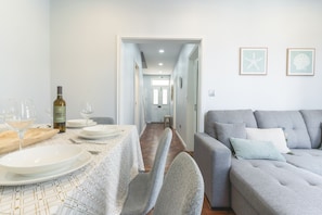 A dining area with a table set for two, a bottle of wine, and two glasses. A grey sofa and a framed picture are visible in the background. - Chez Agostinha by Atlantic Holiday (Funchal)