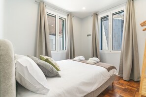 A bedroom with a bed, pillows, a bedside table, and a window with curtains. - Chez Agostinha by Atlantic Holiday (Funchal)