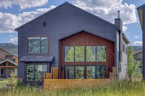A modern two-story house with large windows and a wooden deck. - Big Sky Luxury: Modern 4BR, Heated Patio, Fire Pit, Hot Tub, Views, Walk to Town (Big Sky)