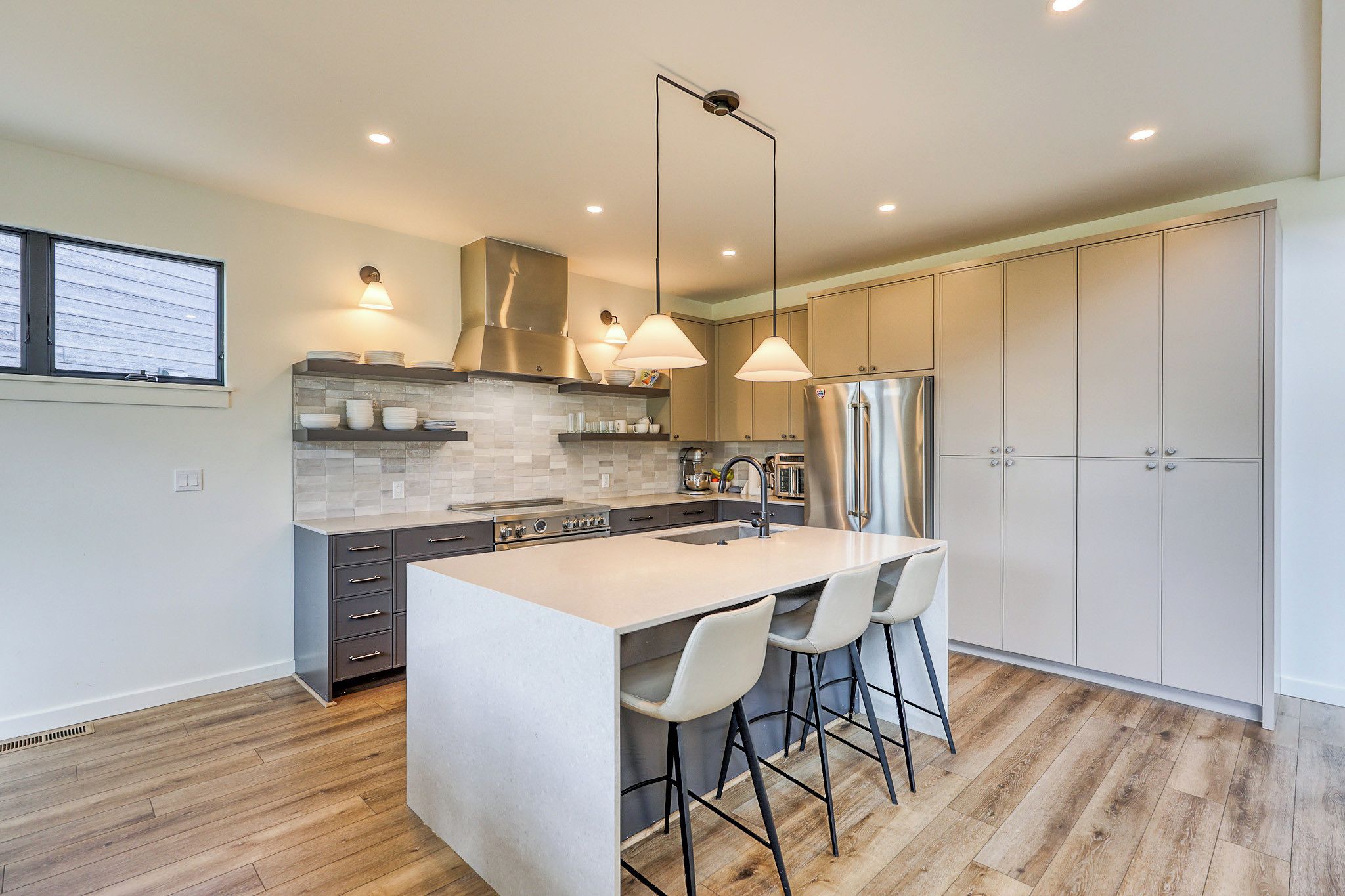 Une cuisine moderne dotée d’un îlot central, de luminaires suspendus et de meubles de rangement intégrés.
