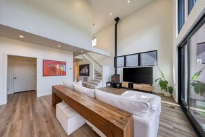 A modern living room with a wooden bench, white sofa, and a large flat-screen TV. - Big Sky Luxury: Modern 4BR, Heated Patio, Fire Pit, Hot Tub, Views, Walk to Town (Big Sky)